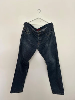 Mörkblå raka jeans med fem fickor - Mörkblå jeans från Zara med klassisk femficksdesign och rak passform. Den lätt tvättade denimen ger en subtil vintagekänsla som passar till både vardag och en mer avslappnad stil. Jeansen har ett hål i skrevet (se bild), vilket är inräknat i priset. I övrigt normalt begagnat skick.