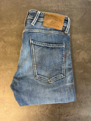 Blå Replay Anbass Jeans, stl 31/34 - Snygga blå jeans från Replay med klassisk femficksmodell och raka ben. Jeansen har en ljus tvätt med subtila slitningar och detaljerad söm på bakfickan. Tillverkade i mjukt denimtyg för en bekväm känsla. NYPRIS: 2000kr
