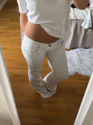 Vita bootcut jeans från Boosley - Säljer ett par vita bootcut jeans från Boosley. Jeansen har låg midja och knappgylf. Perfekta till en trendig och avslappnad stil. Materialet känns mjukt och stretchigt för extra komfort. Uppsydda för kortare ben. (Går att förlänga) Innerbenslängd: 77 cm. Midjemått bredden rakt över när byxorna ligger utlagda: 39 cm. Stl är oklar på etiketten. Bör motsvara XS när jag jmf med andra jeans.