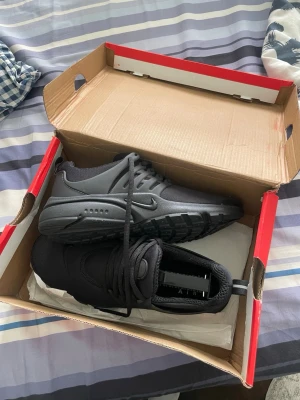 Svarta Nike Air Presto sneakers - Snygga helsvarta Nike Air Presto sneakers med låg profil och klassisk swoosh på sidan. Skorna har en mesh- och syntetöverdel, rund tå och kraftig gummisula för bra grepp. Perfekta för dig som gillar stilrena och sportiga sneakers.