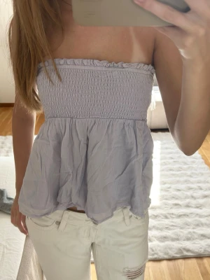 Ljuslila topp - Säljer en söt ljuslila bandeau tubtopp med smockad överdel och volangig nederdel. Toppen är axelbandslös och har en luftig, flowy passform som passar perfekt till sommaren. Står inte storlek men passar mig som har xs