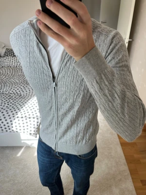 Ljusgrå kabelstickad ziptröja från Massimo Dutti - Säljer en sjukt snygg kabelstickad ziptröja från Massimo Dutti i storleken L. Tröjan är i ett väldigt fint skick utan defekter! ✌🏼——————————————————————————                                                                      📐| Storlek: L                                                           👖| Märke: Massimo Dutti                                      🔎| Skick: Mycket Fint                                                      ✍🏻| Skriv om du har några frågor