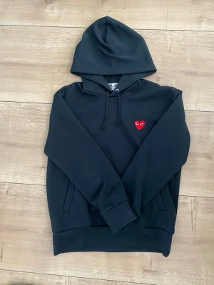 Svart hoodie med rött hjärta - Tröjan är i bra skick utan defekter  och är i storlek m men sitter som en stor m.