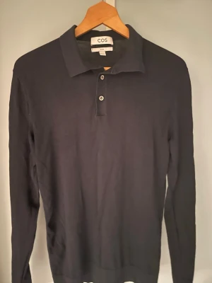 Mörkblå stickad tröja med krage  - Stilren mörkblå långärmad pikétröja från COS med klassisk krage och två knappar framtill. Tillverkad i ett tunt, mjukt material som ger en clean look. Passformen är slim. 