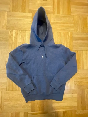 Mörkblå Polo Ralph Lauren hoodie - Snygg mörkblå hoodie från Polo Ralph Lauren med klassisk broderad logga på bröstet. Hoodien har stor huva med dragsko, magficka och ribbade muddar vid ärmar och nederkant. Perfekt för en chill och stilren look.