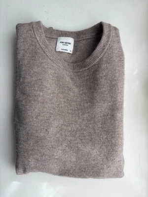 Beige Stickad John Henric - Mysig beige stickad tröja från John Henric i klassisk modell med rund halsringning. Tröjan är tillverkad i kashmir och har ribbade muddar vid ärmslut och nederkant. Perfekt för lager-på-lager och enkel att matcha.