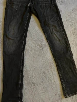 Svarta Replay skinny jeans - Säljer ett par svarta skinny jeans från Replay med slitna detaljer och klassisk femficksmodell. Jeansen har vita kontrastsömmar och är tillverkade i stretchigt denimtyg för en bekväm passform. Perfekta för dig som gillar en smal siluett.
