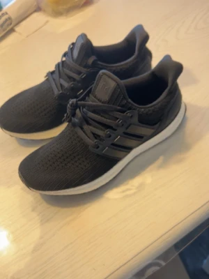 Adidas ultra boost - Snygga svarta sneakers med stickad ovandel och klassiska svarta snören. Skorna har en vit, tjock sula och tre svarta ränder på sidan. Perfekta för dig som gillar sportig och clean stil. Ovandelen är i mesh-liknande material för bra andningsförmåga.