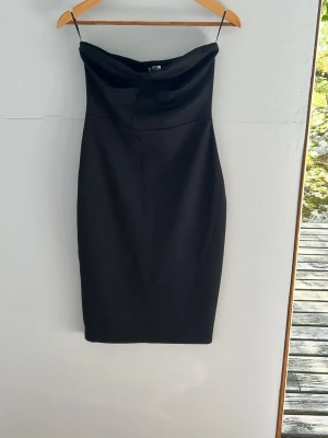 Svart axelbandslös klänning - Snygg svart axelbandslös klänning med figurnära passform och enkel, stilren design. Klänningen har en draperad överdel och smala axelband, perfekt för dig som gillar minimalistisk stil. Materialet känns mjukt och följsamt.