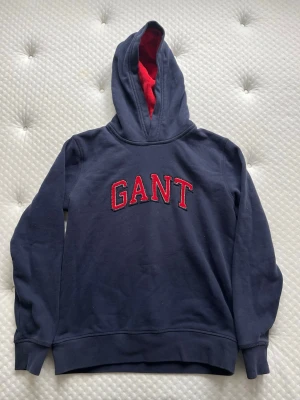 Gant hoodie mörkblå med rött innerfoder - Supersöt gant hoodie i barnstorlek (158-164) hade dock passat en liten herr (XXS), känns som ny och jag har inte kunnat hitta några skavanker. Tröjan är mörkblå med röd logga på bröstet och rött innerfoder i luvan. Materialet är väldigt mjukt och härligt. Tröjan är 90% bomull och 10% polyester. 