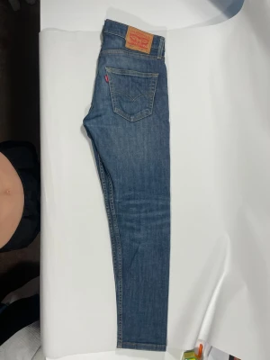 Blå Levi's slim jeans - Säljer ett par klassiska blå slim jeans från Levi's med fem fickor och den ikoniska röda Levi's-lappen på bakfickan. Jeansen har en smal passform och är tillverkade i denim med snygga slitningar för en avslappnad look.