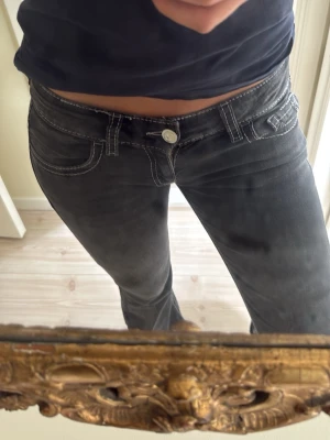Svarta bootcut jeans med vit söm - Säljer ett par svarta bootcut jeans med vita kontrastsömmar och låg midja. Jeansen har klassisk femficksdesign och silverfärgad knapp. Snygg passform som framhäver benen och passar perfekt till en avslappnad stil.