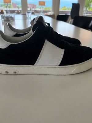 Svarta Valentino Opens 38 - Säljer ett par stilrena Valentino opens i svart och vitt med lågt skaft. Skorna har svart ovandel med vit panel på sidan och vit sula. Klassisk design som passar till det mesta och ger en clean look. Materialet ser ut att vara en mix av mocka och läder.