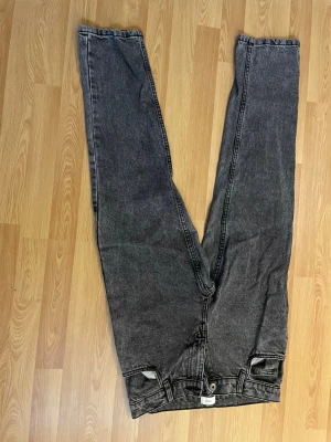Svarta raka jeans med hög midja - Säljer ett par svarta raka jeans med hög midja och klassisk femficksmodell. Jeansen har en tvättad look och raka ben, perfekta för en avslappnad stil. Materialet är denim och de har bälteshällor samt knappgylf.