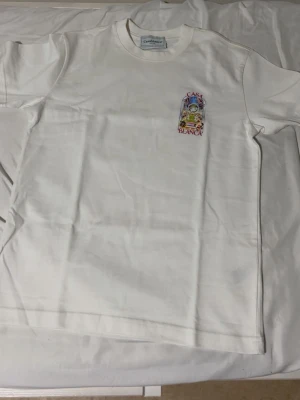 Vit Casa Blanca t-shirt med tryck - Säljer en vit t-shirt från Casa Blanca med färgglatt grafiskt tryck på bröstet och ryggen. T-shirten har rund hals och korta ärmar. Perfekt för dig som gillar unika prints och streetwear-vibe. 