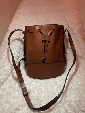 Unused Mango bucket bag 🤎 - Unused brown Mango bucket bag 🤎a stylish, cognac-colored faux leather shoulder bag featuring an adjustable shoulder strap and a drawstring closure. Dimensions are shown in the photos. Material: 100% polyurethane. ✨Also listed on Bought, Tise & Vinted @1233_user
