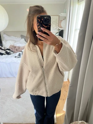 Beige oversized teddyjacka med dragkedja - Mysig och oversized teddyjacka i beige med dragkedja framtill. Jackan har en avslappnad passform, nedhasade axlar och fluffigt material som ger en trendig look. Perfekt för kyliga dagar och enkel att matcha med olika outfits.