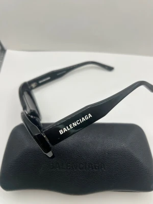 Svarta cat eye-solglasögon Balenciaga - Snygga svarta solglasögon från Balenciaga med cat eye-formade bågar. Glasögonen har en stilren design med Balenciaga-logga på skalmen och kommer med ett matchande svart fodral. Perfekta för dig som vill ha en trendig accessoar.