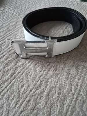 Vitt bälte med silverfärgat spänne - Snyggt vitt bälte med ett stort, silverfärgat spänne i metall. Bältet har en stilren och modern look med svart insida och är perfekt för att lyfta vilken outfit som helst. Passar dig som gillar minimalistisk och clean stil.