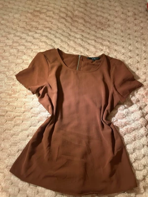 Vinröd  topp från Vero Moda - Säljer en enkel och snygg vinröd topp från Vero Moda. Toppen har rund halsringning, korta ärmar och en synlig dragkedja bak. Materialet känns lätt och luftigt, perfekt för en avslappnad look.