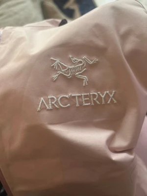 Ljusrosa vindjacka från Arc'teryx - Snygg ljusrosa vindjacka/regnjacka från Arc'teryx med minimalistisk design och diskret logga på ärmen. Jackan har huva, dragkedja framtill och är tillverkad i ett tunt, tekniskt material som skyddar mot vind och lätt regn. Perfekt för dig som gillar stilren outdoor-look. Obs vet ej om jackan är äkta eller ej den är köpt från Vinted 