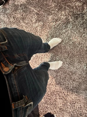 Nudie Jeans - Säljer ett par mörkblå slim fit jeans med klassisk femficksdesign och snygga kontrastsömmar. Jeansen har normal midja och dragkedja med knapp. Perfekta för dig som gillar en stilren och enkel look.