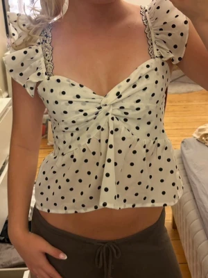 Vit prickig topp med volangärmar - Söt vit topp med svarta prickar och volangärmar. Toppen har en twistad front och lätt v-ringad urringning💗🤩