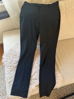 Svarta kostymbyxor  - Snygga svarta kostymbyxor med raka ben och bälteshällor. Insidan av linningen har en röd söm som ger en cool kontrast. Klassisk passform och stilren look, perfekta till skjorta eller t-shirt. Ganska sliten i innertyget men ser nya ut från utsidan🖤