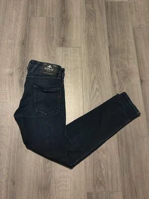 Mörkblå slim fit jeans från Replay - Snygga mörkblå slim fit jeans från Replay med klassisk femficksdesign och diskreta slitningar. Jeansen har en smal passform och är tillverkade i stretchigt denimtyg för extra komfort. Perfekta för dig som gillar en stilren och modern look. De har ingen lapp där storleken står men storleken är W29 L30