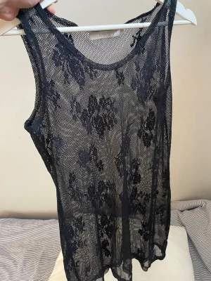 Svart blommig mesh linne/kort klänning - Snygg svart ärmlös linnetopp/ klänning mesh med blommigt mönster. Toppen är transparent och har en ledig passform, perfekt för att styla lager på lager. Passar dig som vill ha en edgy och trendig look.