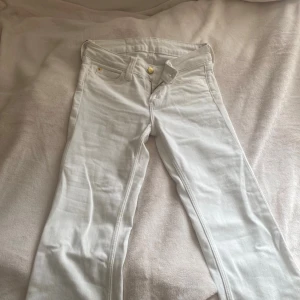 Vita bootcut jeans med tryckdetalj - Snygga vita jeans med bootcut passform och klassiska fem fickor k storlek 26/30. Byxorna har en unik tryckt detalj på linningen baktill som ger en cool touch. Perfekta för dig som vill sticka ut med en stilren men ändå unik look. Har några små fläckar men syns knappt dock en mellan lite grön fläck där bak. 