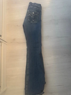 Jeans från Ginatricot  - Säljer ett par blå bootcut jeans med snygga broderier och dekorativa sömmar på bakfickan. Jeansen har klassisk femficksdesign och är gjorda i denim. Passar även en storlek S