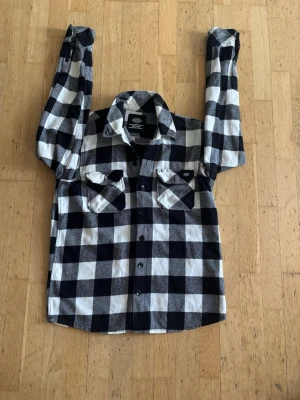 Svartvit rutig skjorta från Dickies - Säljer en klassisk svartvit rutig skjorta från Dickies. Skjortan har två bröstfickor med lock och knappar framtill. Perfekt för dig som gillar en avslappnad och tidlös stil. Materialet känns mjukt och bekvämt, och passformen är normal.