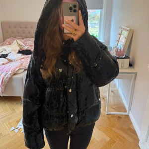 Svart paljett pufferjacka med huva - Säljer en svart pufferjacka med glittriga paljetter. Jättesnygg luva. Nypris nästan 4000kr. Från Ida Sjöstedt. 