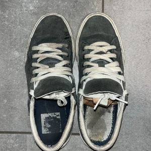 Mörkblå sneakers från Helly Hansen - Snygga mörkblå sneakers från Helly Hansen med vit platt sula. Snörerna skulle behöva en tvätt. Ovandelen är i mocka och insidan har en mjuk textil. Skorna har rund tå och klassisk låg profil, perfekt för en chill streetstil. Helly Hansen-logga på sulan och sidan.