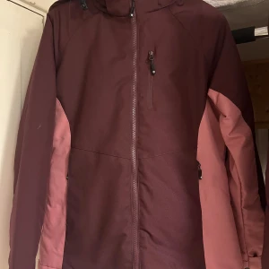 Vinröd vindjacka från Ski Industries - Säljer en vinröd vindjacka från Ski Industries i storlek M. Jackan har huva, dragkedja framtill och praktiska fickor med dragkedja. Materialet är vindtätt och vattenavvisande, perfekt för kalla dagar. Snygga kontrastpaneler i mörkrött och rödrosa på ärmarna.