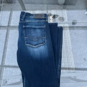 🌀 Replay Jeans – Modell ANBASS (32) - Snygga och klassiska jeans från Replay, modell ANBASS i storlek 32. Slim fit med lätt stretch för perfekt passform och komfort. Mörkblå tvätt med snygga slitningar som ger en exklusiv, använd look. Kvaliteten är riktigt bra – jeansen är i fint skick utan hål eller fläckar. Perfekta för både vardag och kväll, matchas lika bra med sneakers som med skjorta.  👖 Modell: Replay Anbass 📏 Storlek: 32 🎨 Färg: Mörkblå / tvättad denim 💎 Skick: Mycket bra 💰 Nypris ca 1500–1800 kr  