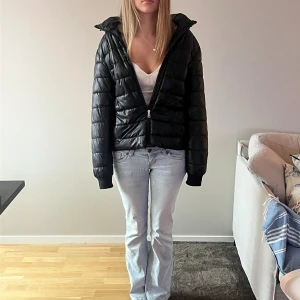 Svart pufferjacka med huva - Säljer en svart pufferjacka med huva och dragkedja framtill. Jackan har quiltad design och långa ärmar med muddar. Perfekt för dig som vill ha en stilren och varm jacka med loose passform. Enkel att matcha med jeans eller hoodies.