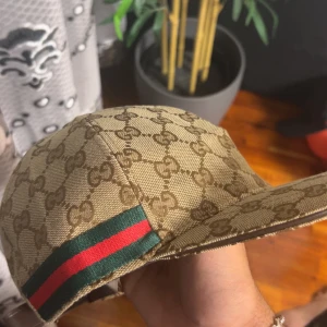 Gucci keps med GG-mönster och röd/grön detalj - Snygg beige keps från Gucci med klassiskt GG-monogram över hela ytan och en ikonisk röd/grön rand på sidan. Helt nya oanvänd kommer med tags och dustpåse 