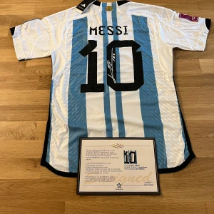 Signerad Messi Argentina matchtröja - Exklusiv Argentina fotbollströja från Adidas med Messis namn och nummer 10, signerad av Messi. Tröjan har klassiska blå och vita ränder, svarta detaljer och officiella VM-märken. Tillverkad i lätt funktionsmaterial med HEAT.RDY-teknologi.
