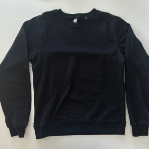 Svart sweatshirt från Clique, stl S - En stilren svart sweatshirt från Clique i storlek S. Tröjan har rund hals, ribbade muddar vid ärmslut och nederkant samt lång ärm. Materialet är mjuk bomull med insida i fleece för extra komfort. Perfekt för chill dagar eller när du vill ha en enkel look.