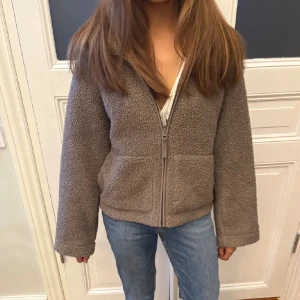 Brun teddyjacka med dragkedja - Mysig brun teddyjacka med dragkedja framtill och två stora fickor. Jackan har en loose passform och är tillverkad i mjukt fleece-material som håller dig varm. Storlek xs men skulle säga att den är mer s