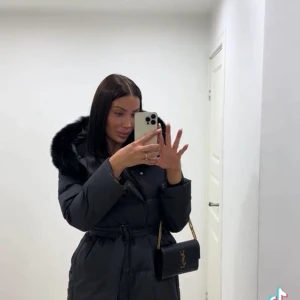 Svart dunjacka med fuskpäls och bälte - Säljer en svart dunjacka med fluffig fuskpäls på huvan och bälte i midjan för snygg passform. Passar även M. Från FurStockholm