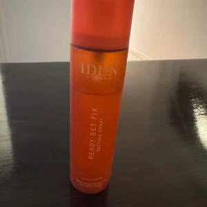 IDUN Minerals Ready Set Fix Setting Spray - Fräsch orange setting spray från IDUN Minerals, Ready Set Fix. Ger ultra fixering och en naturlig glow till din makeup. Kommer i en snygg cylinderformad plastflaska med sprayfunktion. Perfekt för att hålla sminket på plats hela dagen. Endast testad.