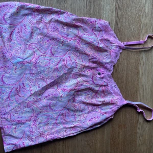 Paisleymönstrad lila linnetopp med spets - Säljer en söt linnetopp med paisleymönster i lila, rosa och blå toner. Toppen har tunna justerbara axelband med glitter och spetskant upptill samt en liten rosett framtill. Går både att sova i eller matcha till ett par jeans!💗