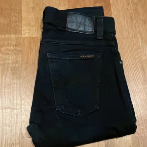 Svarta Tight Terry Nudie Jeans - Säljer ett par svarta Nudie Jeans Tight Terry med klassisk femficksdesign och snygga svarta sömmar. Jeansen är tillverkade av 98% bomull och 2% elastan för en skön och tight passform. Märkespatch i svart på bakfickan och diskret broderad logga. Pris kan diskuteras vid snabb affär!