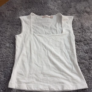 Vit linnetopp från Gina Tricot - Säljer en stilren vit linnetopp från Gina Tricot med fyrkantig urringning. Toppen är ärmlös och gjord i mjuk bomull, perfekt för varma dagar eller att styla med lager. Enkel och clean design som passar till många outfits.