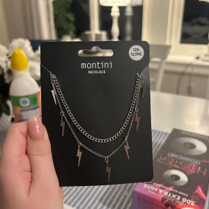 Montini halsband med blixtberlocker - Dubbelkedjat halsband i silverfärg från Montini med coola blixtformade berlocker. Kedjorna har olika längd för en lager-på-lager-effekt och ger en edgy vibe till din stil. Perfekt accessoar för dig som gillar detaljer som sticker ut.