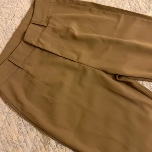 Beiga kostymbyxor med hög midja - Stilrena beiga kostymbyxor med hög midja och raka ben. Byxorna har bälteshällor och dold stängning framtill. Materialet känns mjukt och har ett snyggt fall. Står storlek s men skulle säga att det är mer M/L