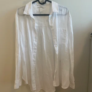 Vit linneskjorta med knappar - Luftig vit skjorta i linne från H&M med klassisk krage och knäppning framtill. Skjortan har lång ärm och en bröstficka.